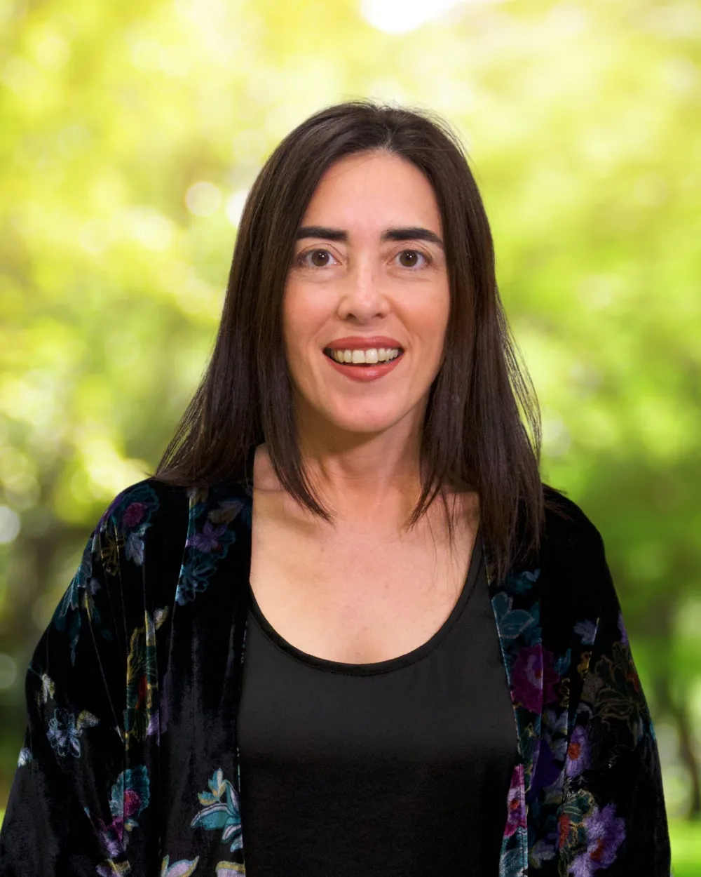 Dayana Pereira smiling against a green nature background.